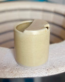 Pale yellow ceramic to-go cup on a kiln edge