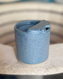 Blue speckled ceramic to-go cup on a kiln edge